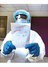 穿著白色防護衣的護理師方秀能，以書寫方式向病患說明他的血壓、心跳、體溫等生命體徵，讓病患了解自己的病況。（圖／高榮臺南分院）之照片